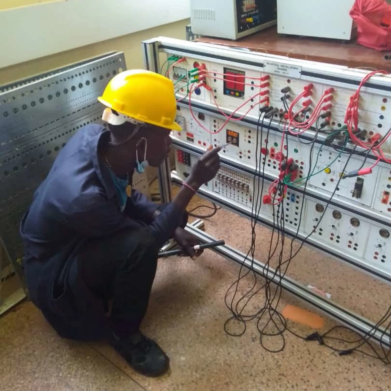 Auszubildender mit Schutzhelm an einer Elektronik-Schaltwand