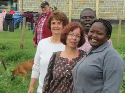 Zwei Malaika-Mitarbeiter und zwei Reisende stehen gemeinsam auf der begrünten Anbaufläche des Malaika Children’s Home, im Hintergrund ist Willy Schneider zu sehen.
