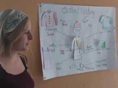 Amelie Herlan bringt den Kinder deutsche Wörter zum Thema Kleidung mit einem Lernplakat bei.