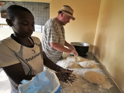Togo und ein Malaika Kind kneten gemeinsam den Teig für das Ugali Brot.