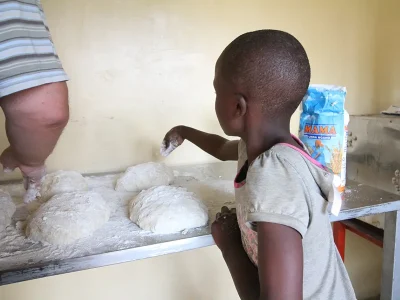 Ein Malaika Kind bestreut das Ugali Brot mit Mehl.