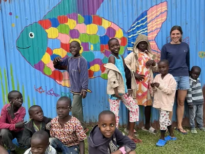 Laura steht mit einer Gruppe von Kindern vor dem buten Regenbogenfisch der auf den Zaun gemalt ist