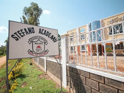 Stefano Academy Malaika Schule Schild mit Schulgebäude im Hintergrund