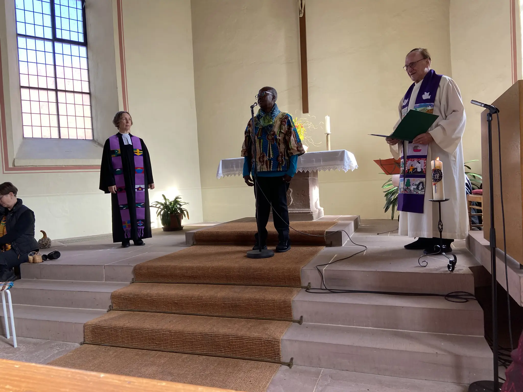 Asuna Schneider erzählt vor dem Altar zwischen den Pfarrern Willy Schneider und Marco Rückert.