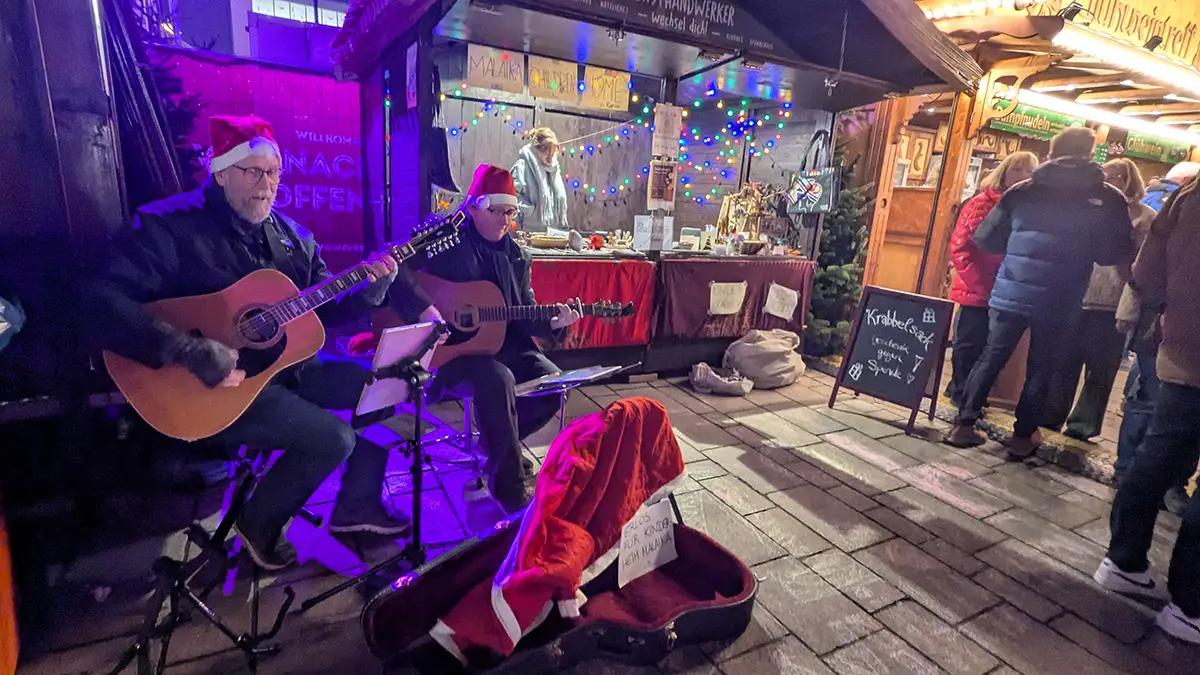 Stefan und sein Kollege spielen Gitarre für Malaika auf dem Weihnachtsmarktstand in Offenburg