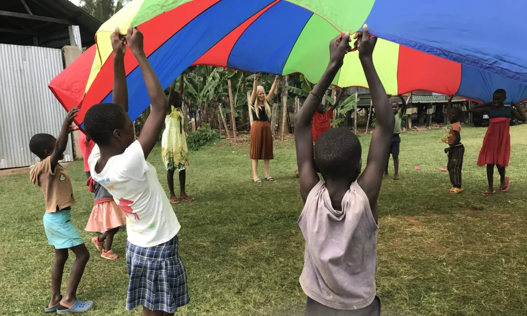 Amelie Herlan und die Kinder schwingen gemeinsam ein großes Regenbogen-Tuch in die Luft.