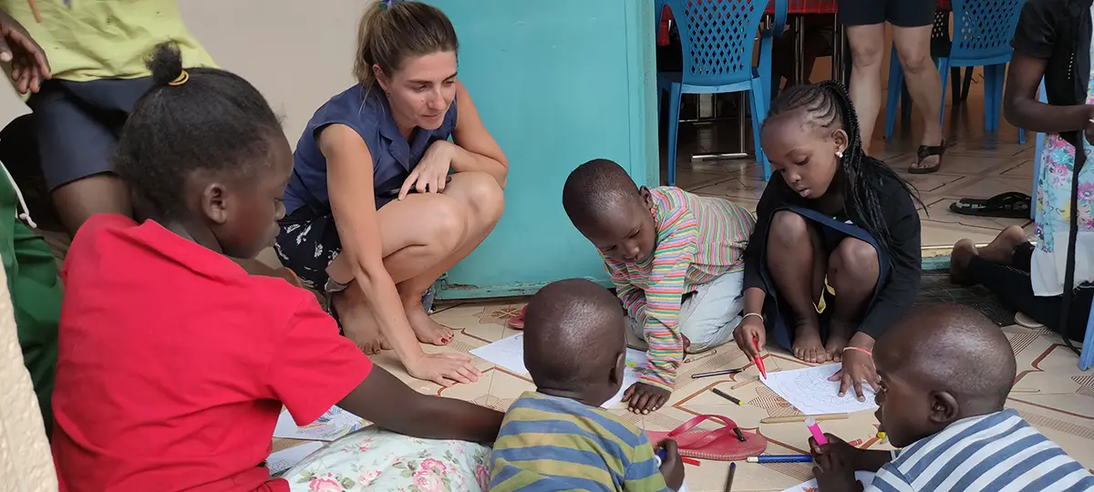 Laura sitzt mit einigen Kindern auf dem Boden. Sie zeichnen gemeinsam.