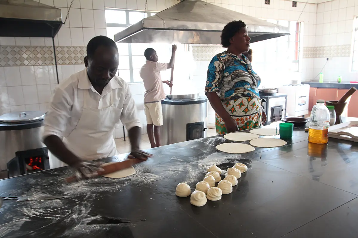 Mark bereitet mit der Küchencrew Chapati-Teig in der Malaika-Küche zu, während im Hintergrund Ugali gerührt wird.