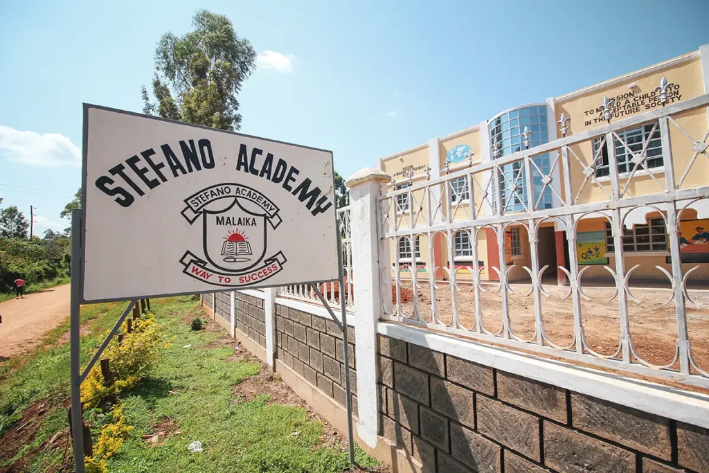 Stefano Academy Malaika Schule Schild mit Schulgebäude im Hintergrund