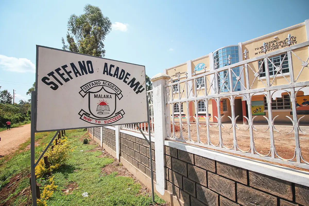 Stefano Academy Malaika Schule Schild mit Schulgebäude im Hintergrund